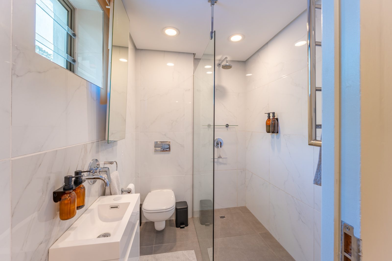 Second bathroom with a walk-in glass shower, wall-hung toilet and marble-look tiles